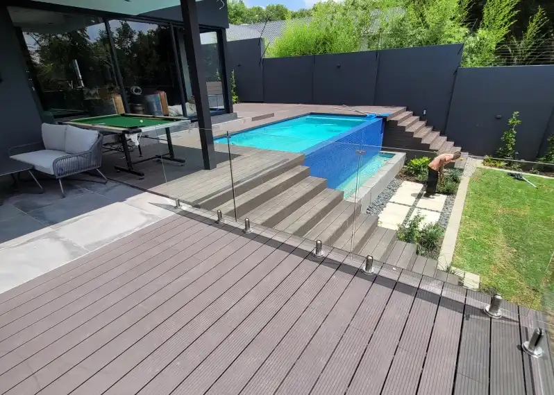 Premium composite decking installed around a modern swimming pool with outdoor entertainment area and glass balustrades.